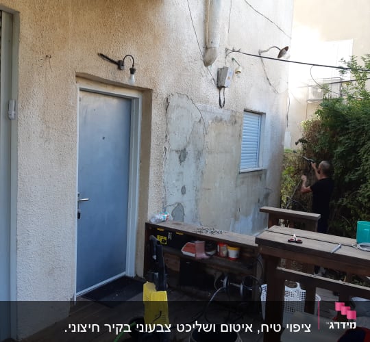 אדם משתמש במכשיר לחץ מים לניקוי קיר חיצוני